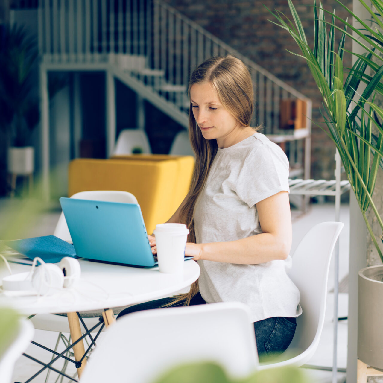 A woman working remotely on a computer at a desk by the window in a cafe. A woman working remotely on a computer at a desk by the window in a cafe. Communicate wirelessly on social media and chat.